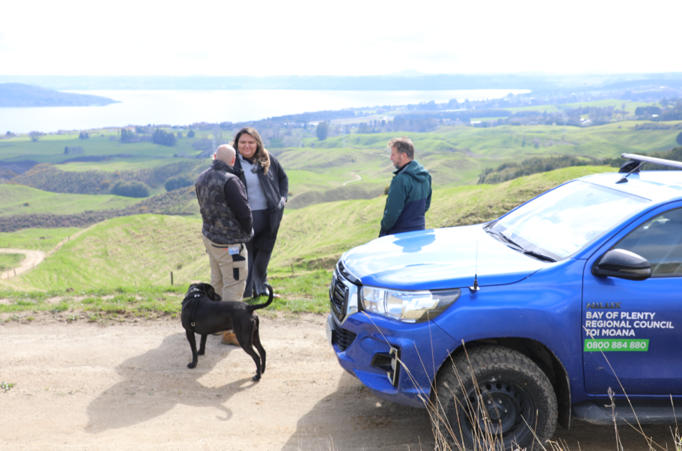 Three people standing by vehicle discussing project works